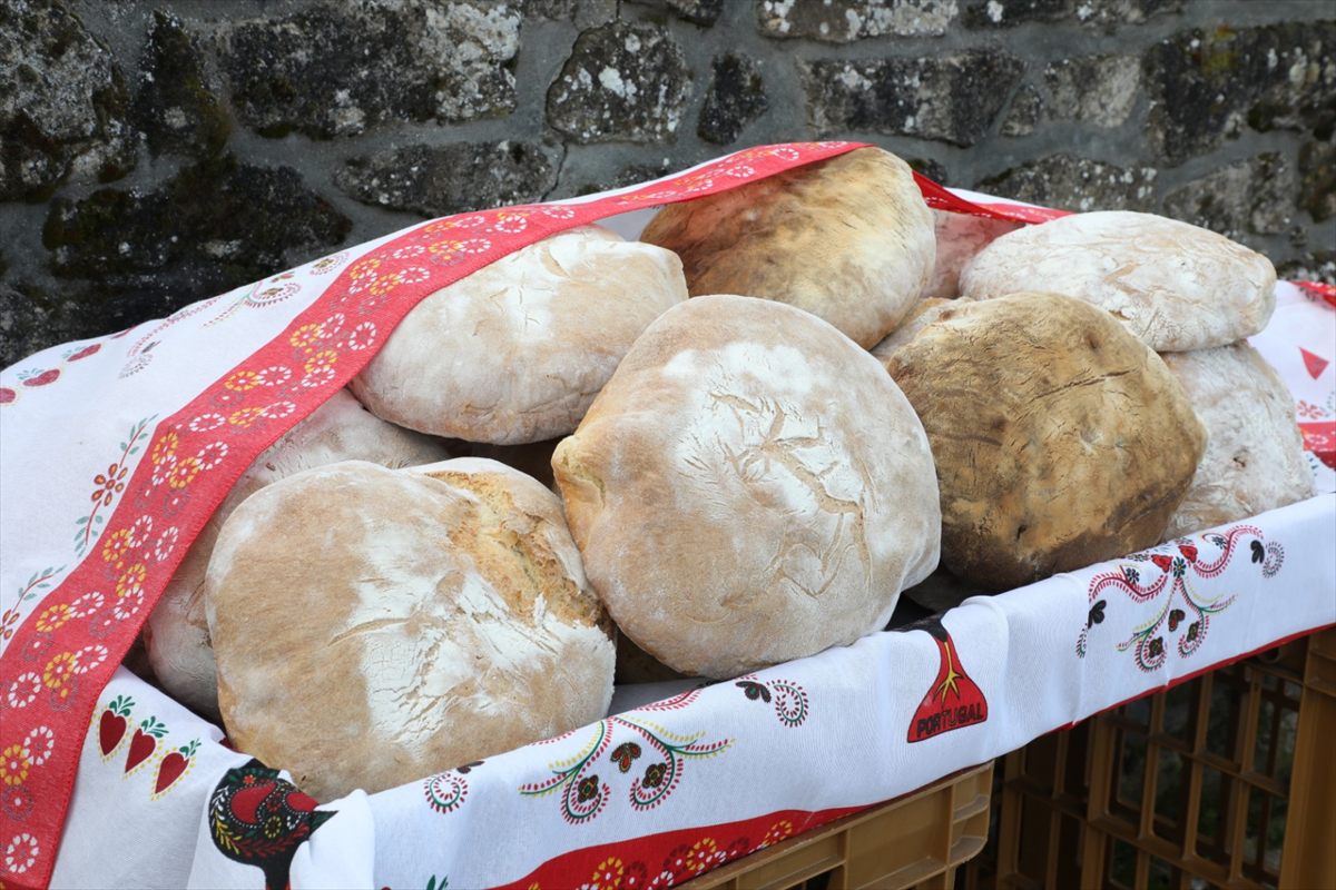 Broas de pão cozido sobre uma toalha bordada, encostadas a um muro de pedra, na Feira do Pão