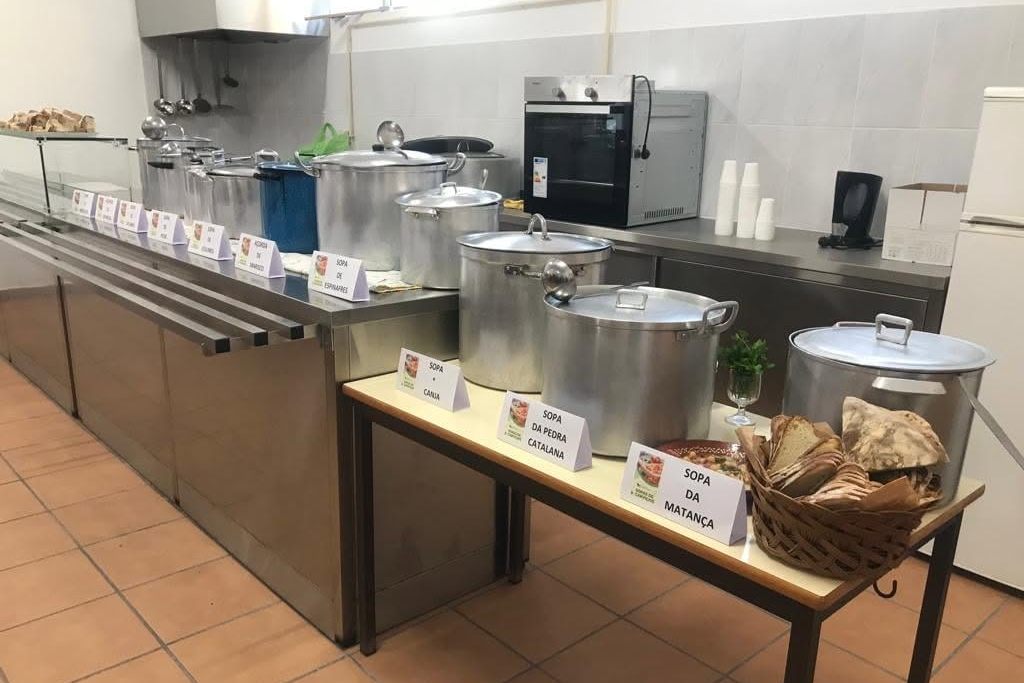 Panelas de sopa alinhadas com as etiquetas Sopa da Casa, Sopa da Pedra Catalana e Sopa da Matança, e um cesto de pão